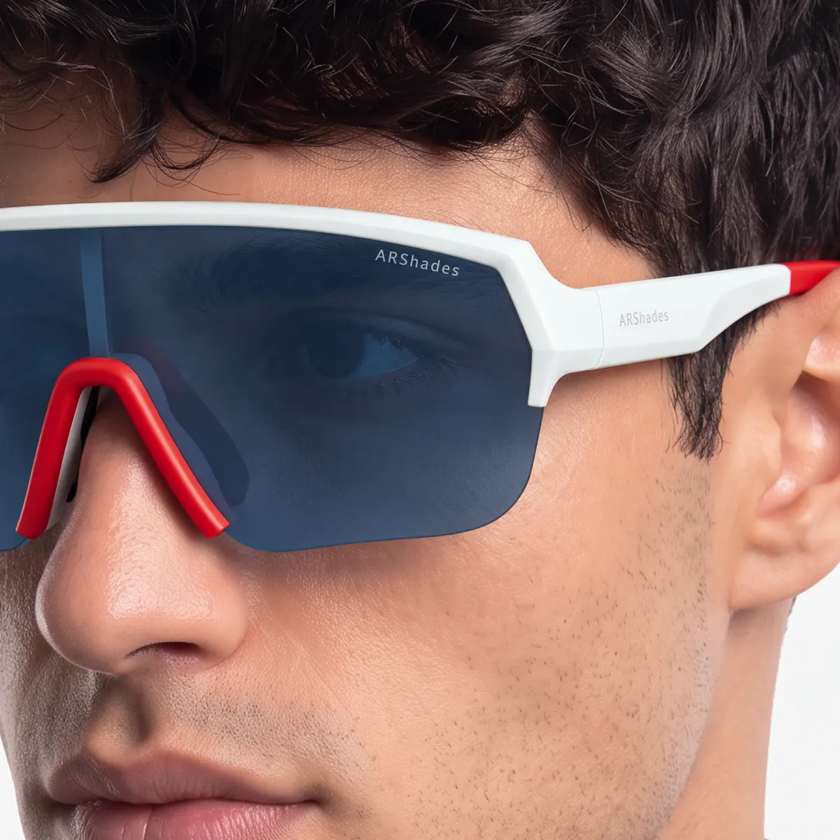 Close-up of someone wearing Airstorm sports shield glasses: white frame with a red bridge and a blue mirrored lens, with the ARShades lettering sharp and legible on the lens and temple.